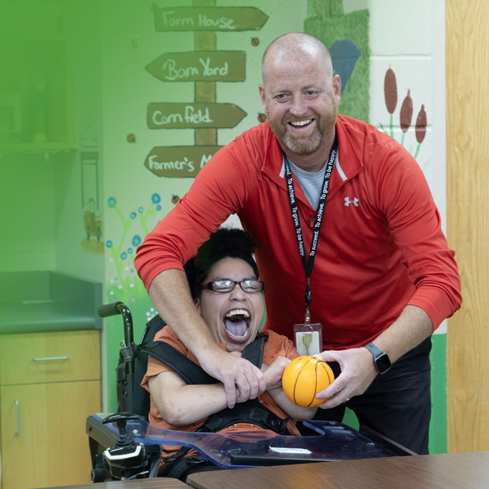 man helping another man in a wheelchair hold a ball